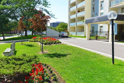 a city street with an apartment building and a park with flowers